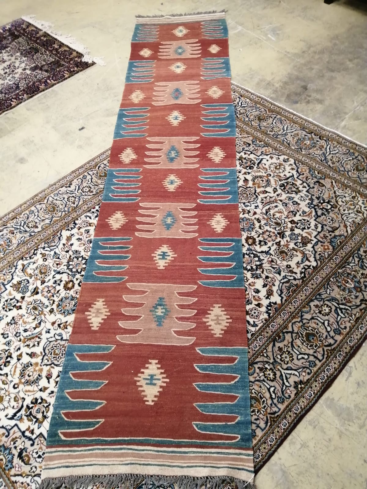A Kilim runner with geometric motifs on a brick red ground, 384 x 85cm